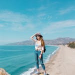 Woman standing on a bluff overlooking a beautiful beach and ocean in sunny weather.